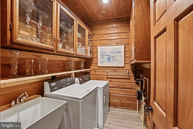 laundry area featuring cabinets, washer and clothes dryer, sink, and wood walls