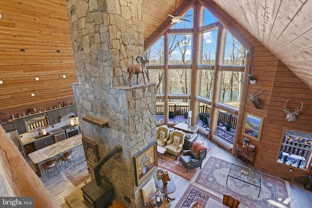 unfurnished living room with wood walls, high vaulted ceiling, wooden ceiling, ceiling fan, and hardwood / wood-style floors