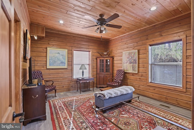 living area featuring hardwood / wood-style flooring, ceiling fan, wood walls, and wooden ceiling