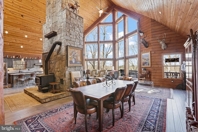 dining room featuring wood walls, a wood stove, hardwood / wood-style flooring, ceiling fan, and wooden ceiling