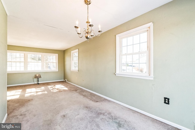 spare room featuring carpet, a wealth of natural light, and an inviting chandelier