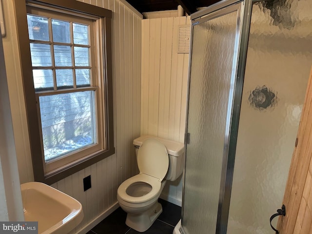 bathroom with toilet, wooden walls, tile patterned flooring, and a shower with door