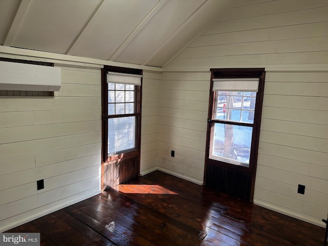 spare room featuring vaulted ceiling, dark hardwood / wood-style floors, a healthy amount of sunlight, and wood walls