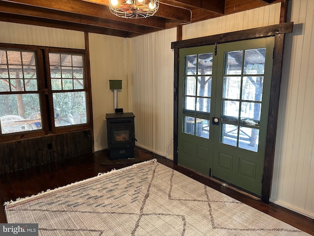 foyer featuring dark wood-type flooring, wood walls, a wood stove, a notable chandelier, and beam ceiling