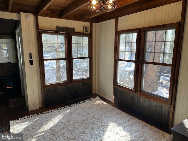 interior space with beamed ceiling, a chandelier, wood ceiling, and wood walls