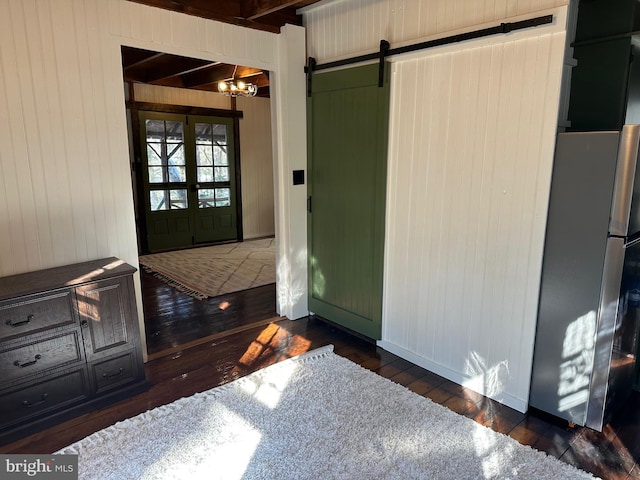 interior space featuring french doors, an inviting chandelier, wooden walls, dark hardwood / wood-style flooring, and a barn door