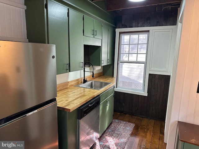 kitchen featuring green cabinets, stainless steel appliances, wooden walls, and sink