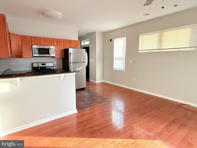 kitchen with dark hardwood / wood-style flooring, a breakfast bar area, stainless steel appliances, and ceiling fan