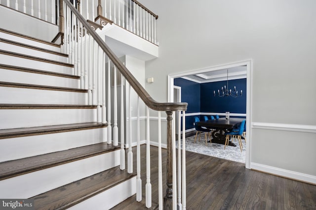 stairway featuring wood-type flooring, a chandelier, and a high ceiling