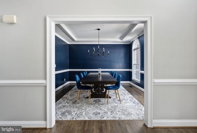 dining area with a raised ceiling, hardwood / wood-style floors, and a notable chandelier