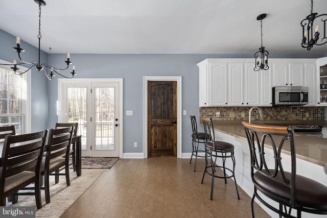 kitchen featuring pendant lighting, an inviting chandelier, white cabinets, a kitchen bar, and decorative backsplash