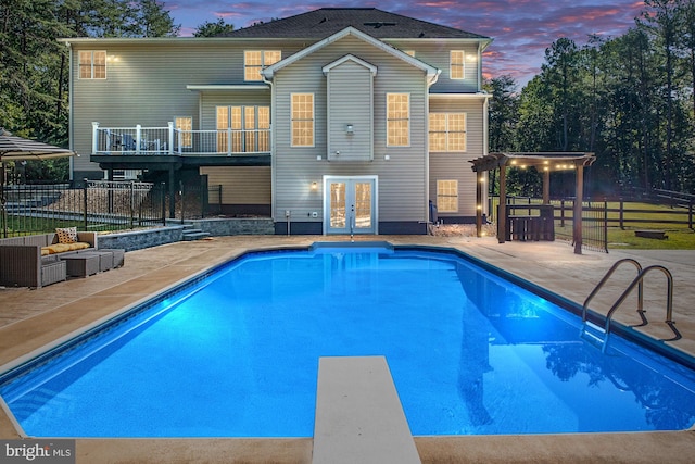 pool at dusk with a pergola, a patio area, a diving board, and french doors