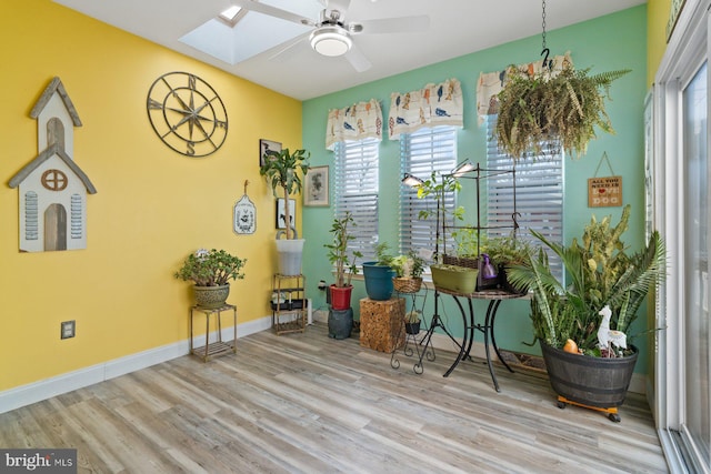 living area with a skylight, ceiling fan, baseboards, and wood finished floors