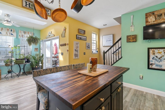 dining area with a skylight, stairway, light wood-style floors, ceiling fan, and baseboards