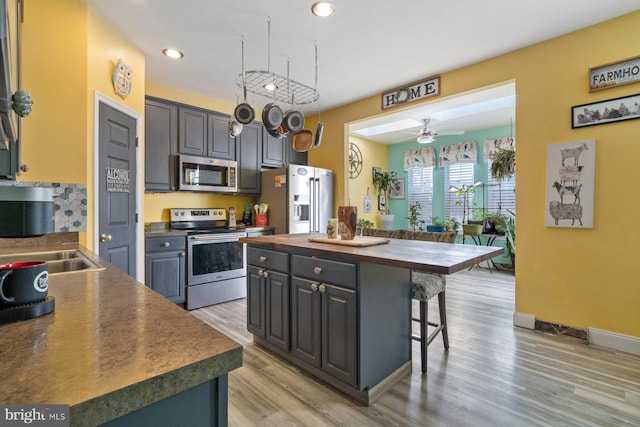 kitchen with a breakfast bar area, a kitchen island, wood counters, appliances with stainless steel finishes, and light wood finished floors