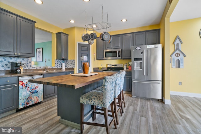 kitchen with a kitchen island, appliances with stainless steel finishes, a breakfast bar, wooden counters, and a sink