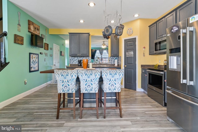 kitchen with tasteful backsplash, baseboards, appliances with stainless steel finishes, a breakfast bar, and light wood-type flooring