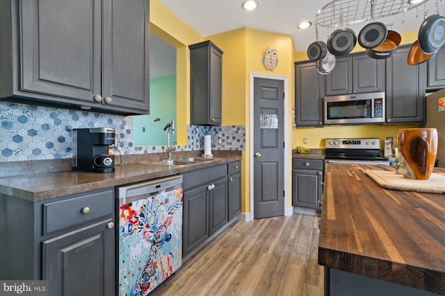 kitchen featuring light wood finished floors, tasteful backsplash, butcher block counters, appliances with stainless steel finishes, and a sink