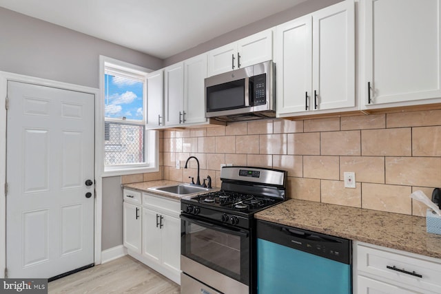 kitchen featuring appliances with stainless steel finishes, tasteful backsplash, sink, white cabinets, and light stone countertops