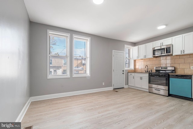 kitchen with white cabinetry, backsplash, light wood-type flooring, and appliances with stainless steel finishes