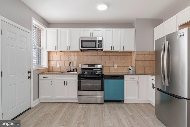 kitchen with stainless steel appliances, white cabinetry, sink, and dark stone countertops