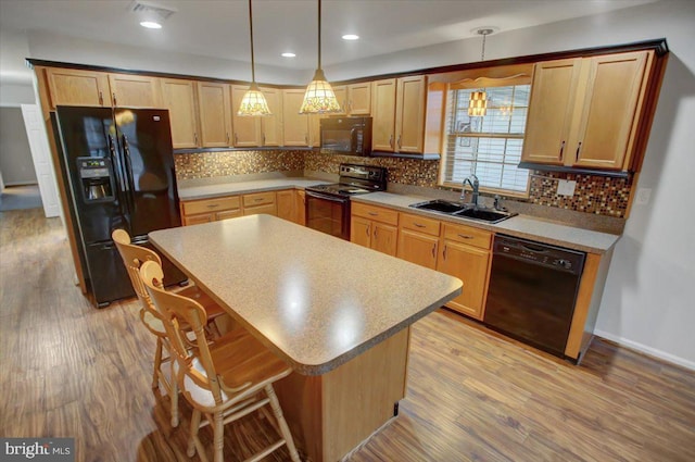 kitchen featuring sink, a breakfast bar area, hanging light fixtures, a center island, and black appliances