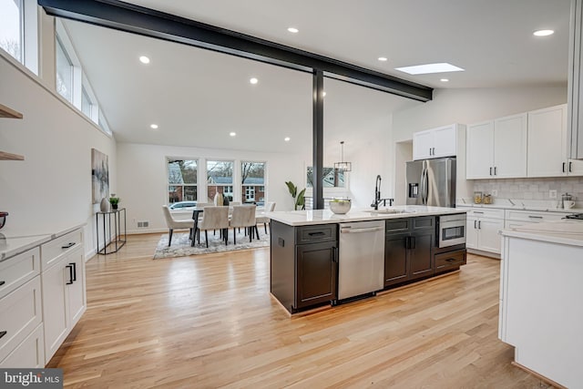 kitchen featuring sink, a center island with sink, light wood-type flooring, stainless steel appliances, and white cabinets