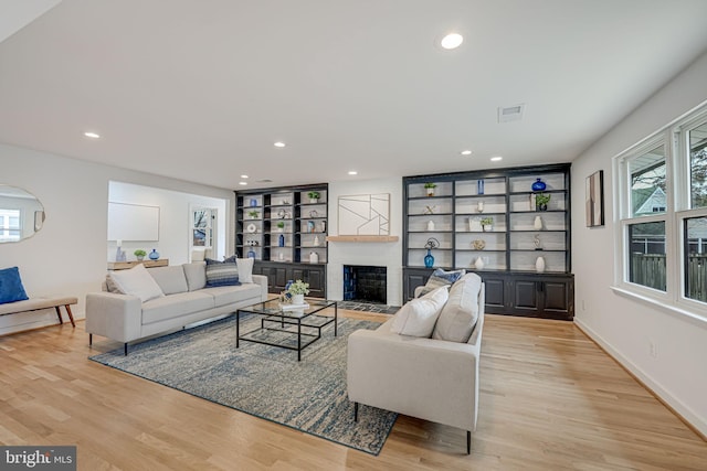 living room featuring light hardwood / wood-style flooring, a fireplace, built in shelves, and a wealth of natural light