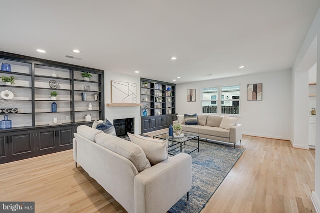 living room featuring a brick fireplace, built in features, and light hardwood / wood-style floors