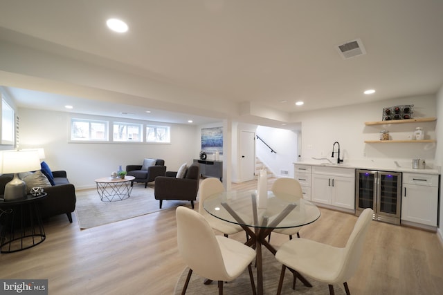 dining space with beverage cooler, indoor wet bar, and light wood-type flooring