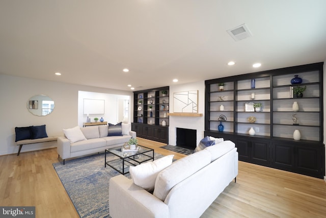 living room featuring built in shelves, a fireplace, and light hardwood / wood-style floors