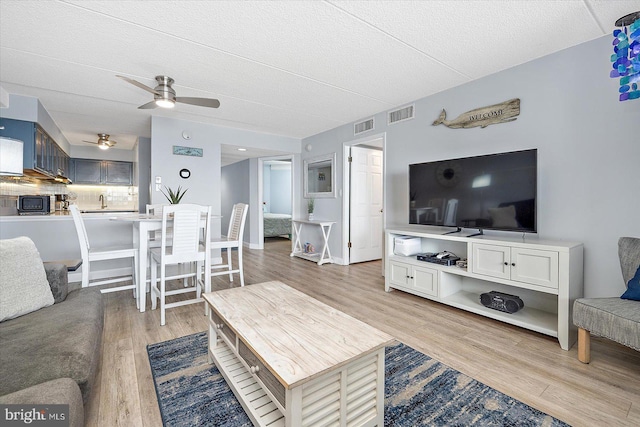 living room with ceiling fan, a textured ceiling, and light wood-type flooring