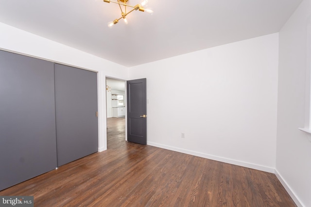 unfurnished bedroom with dark hardwood / wood-style flooring, a closet, and an inviting chandelier