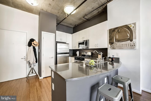 kitchen with appliances with stainless steel finishes, white cabinets, light hardwood / wood-style floors, and kitchen peninsula