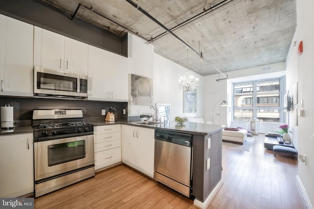 kitchen with white cabinetry, decorative light fixtures, stainless steel appliances, and light hardwood / wood-style floors