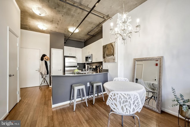 kitchen with white cabinetry, appliances with stainless steel finishes, kitchen peninsula, pendant lighting, and hardwood / wood-style floors