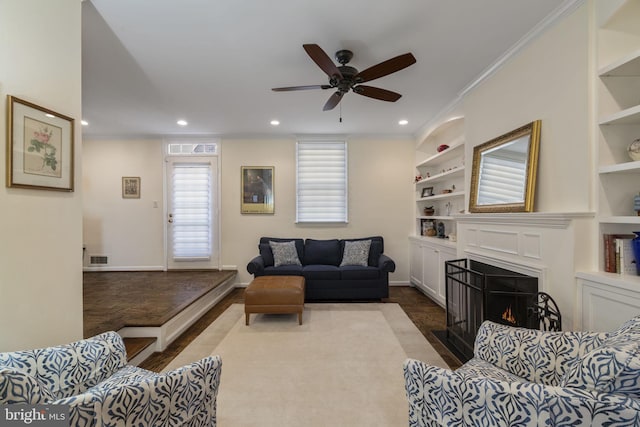 living room featuring built in shelves, ceiling fan, and ornamental molding