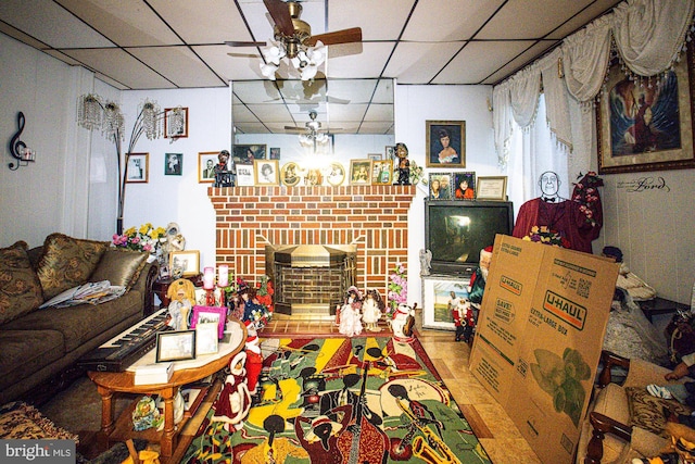 living room with ceiling fan, a paneled ceiling, and a brick fireplace