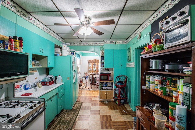 kitchen with fridge, white range with gas cooktop, a drop ceiling, and ceiling fan