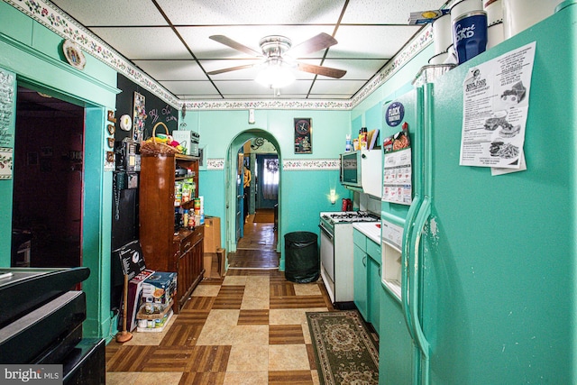 kitchen featuring a paneled ceiling, white range with gas stovetop, refrigerator with ice dispenser, and ceiling fan