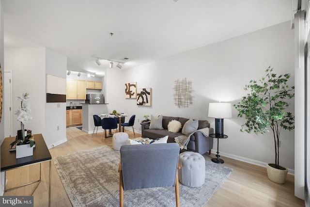 living room featuring light wood-style floors, track lighting, visible vents, and baseboards