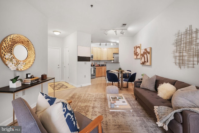 living area with light wood-type flooring, rail lighting, visible vents, and baseboards