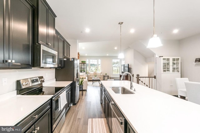 kitchen with stainless steel appliances, decorative light fixtures, sink, and light hardwood / wood-style flooring