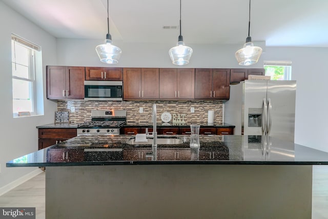 3603 Oakmont Ave, Baltimore, MD 21215 - kitchen featuring appliances with stainless steel finishes, a kitchen island with sink, backsplash, a sink, and decorative light fixtures