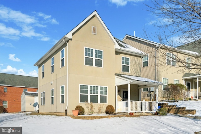 snow covered back of property featuring a porch