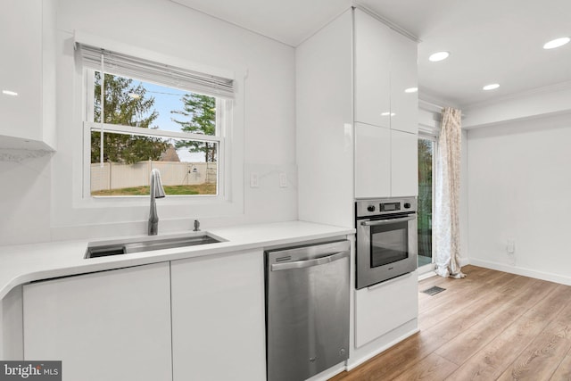 kitchen featuring sink, white cabinets, stainless steel appliances, plenty of natural light, and light hardwood / wood-style flooring