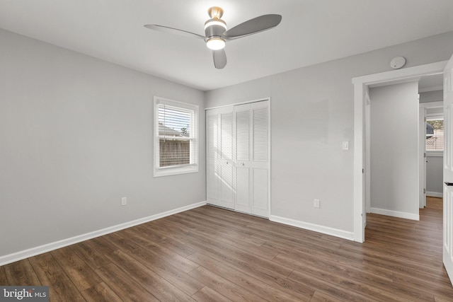 unfurnished bedroom featuring multiple windows, dark hardwood / wood-style flooring, a closet, and ceiling fan