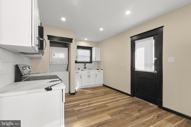 kitchen with stacked washer / dryer, light stone countertops, light hardwood / wood-style floors, decorative backsplash, and white cabinets