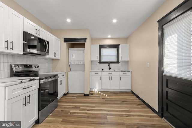 kitchen featuring sink, hardwood / wood-style flooring, stainless steel appliances, stacked washing maching and dryer, and white cabinets