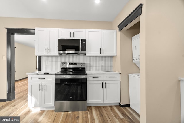 kitchen featuring appliances with stainless steel finishes, white cabinetry, tasteful backsplash, stacked washer / drying machine, and light wood-type flooring